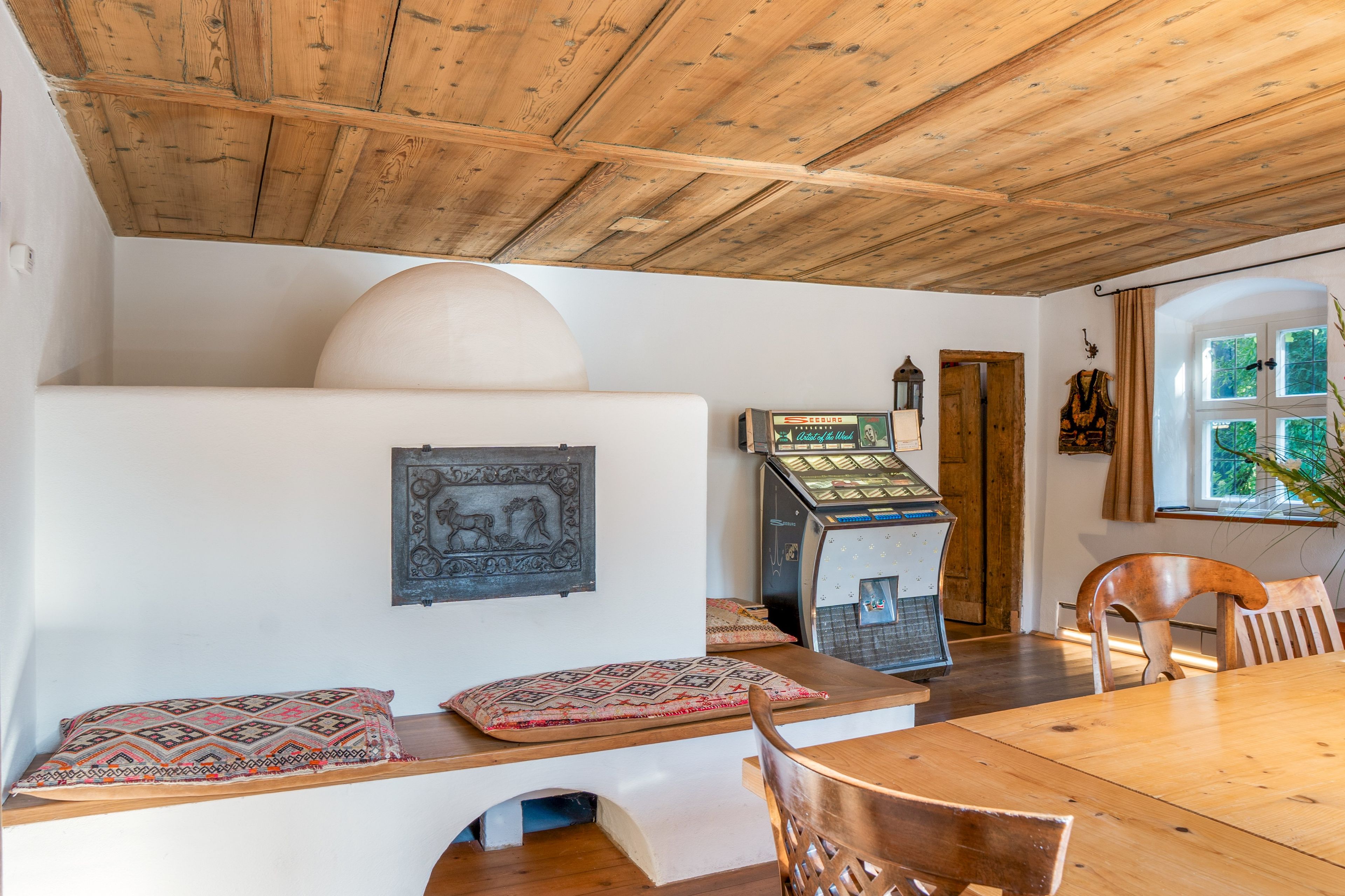 Ein Essbereich mit Holztisch und Stühlen, einem dekorativen Wandelement und einem Vintage-Jukebox.