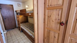 Une pièce avec un lit superposé, une armoire en bois et une porte.