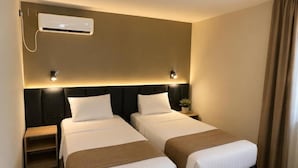 A hotel room with two beds, a wall-mounted air conditioner, bedside lamps, a small table with a plant, and a window with curtains. - Hotel Bellevue (Ilinden)