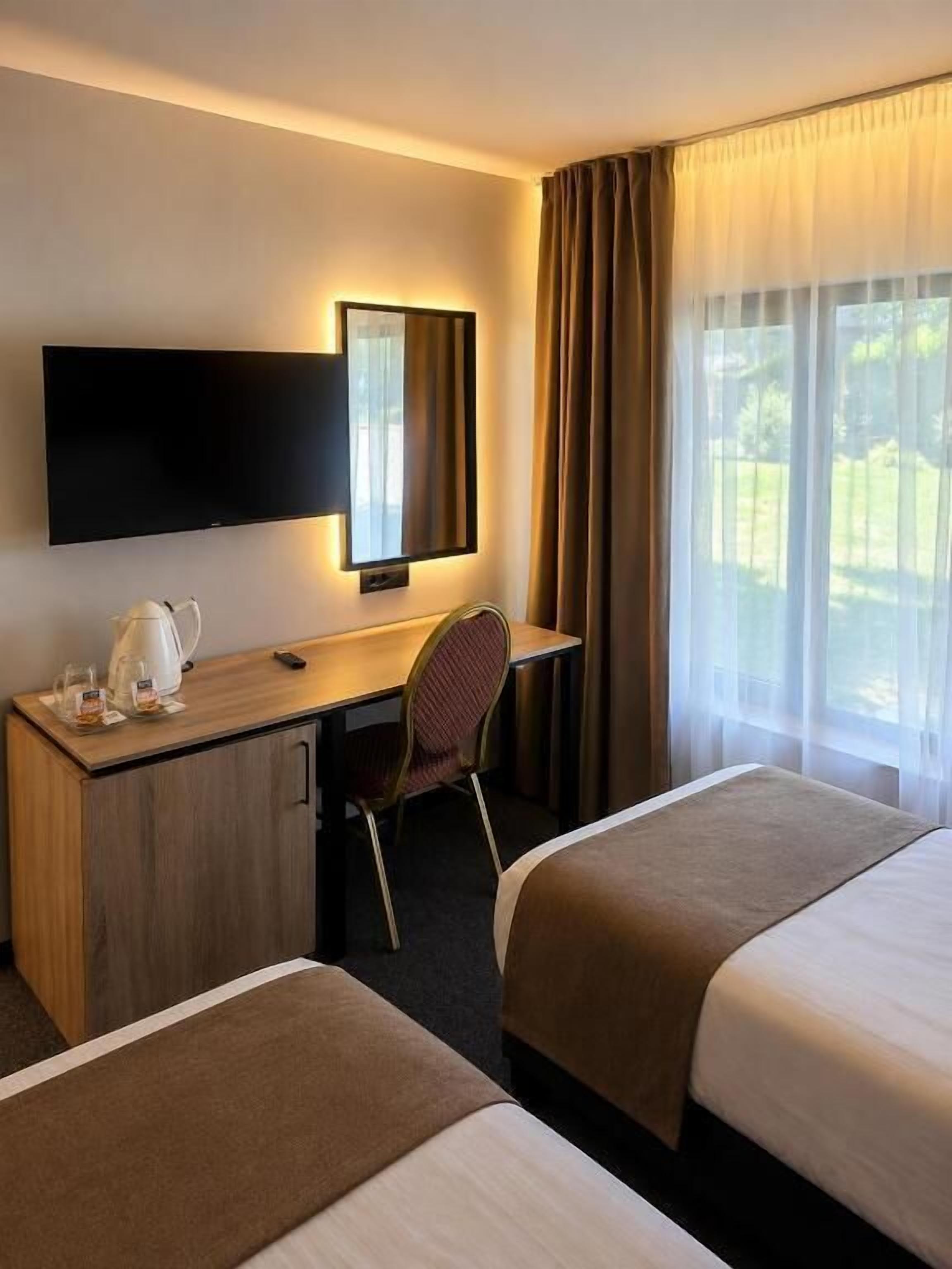 Habitación de hotel con cama, escritorio, silla, televisor y ventana con cortinas.