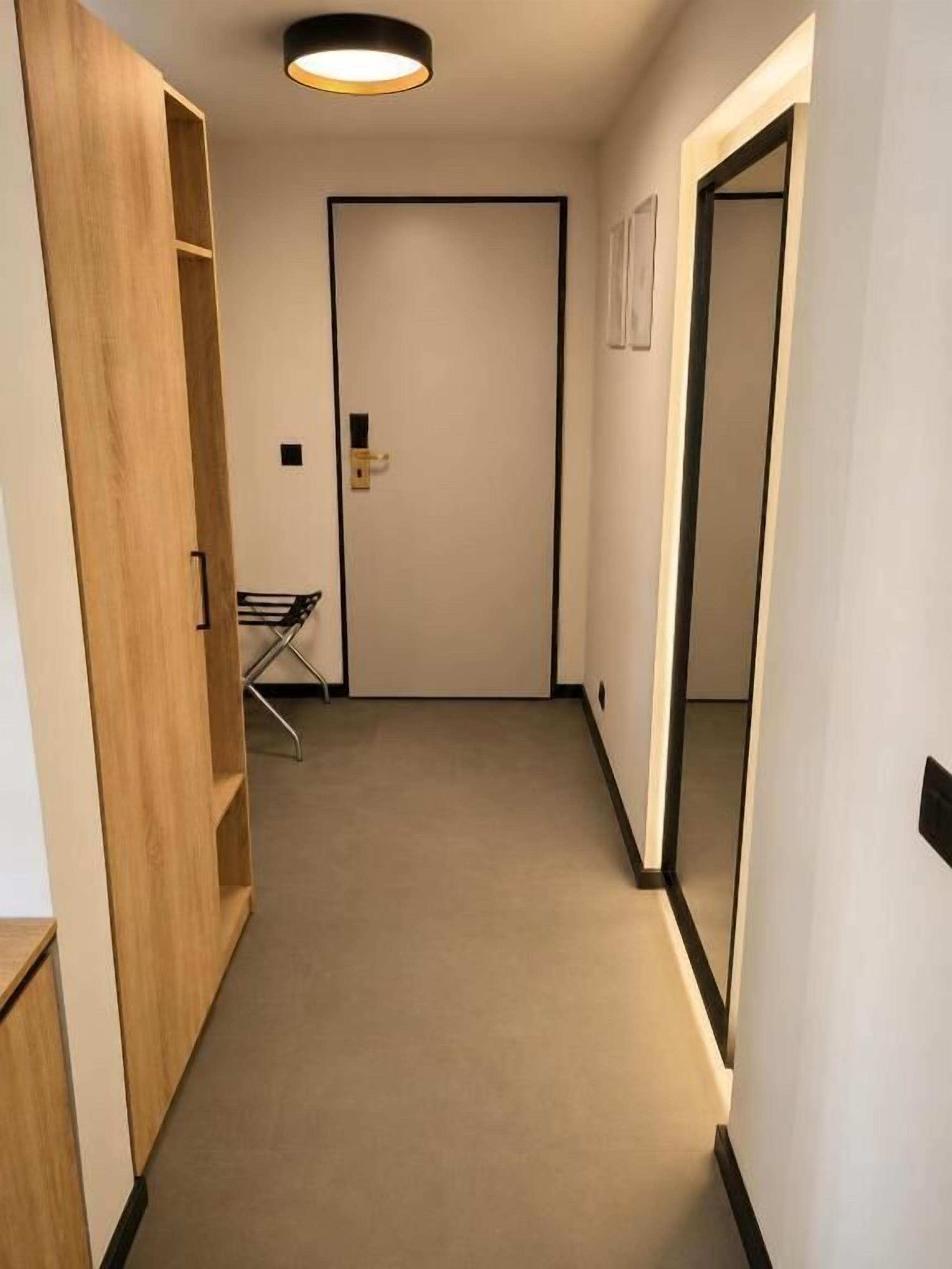 Un pasillo estrecho con un armario de madera, una puerta con manija y un pequeño perchero con objetos.