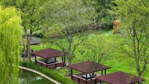 A view of a park with trees, a pond, and wooden gazebos. - Hotel Bellevue (Ilinden)