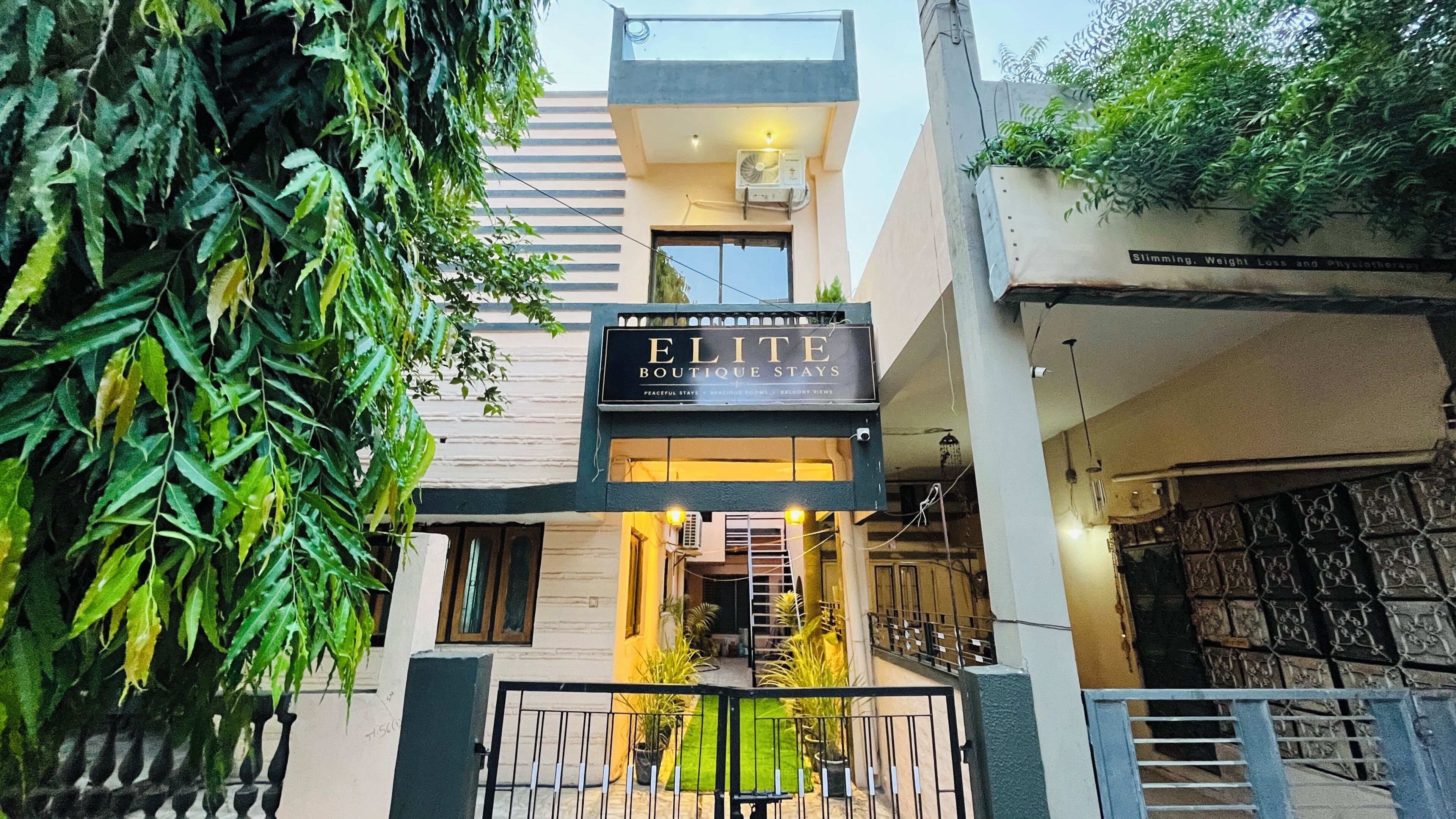 A boutique hotel named 'ELITE BOUTIQUE STAYS' with a signboard, a staircase leading to the entrance, and a gated entrance.