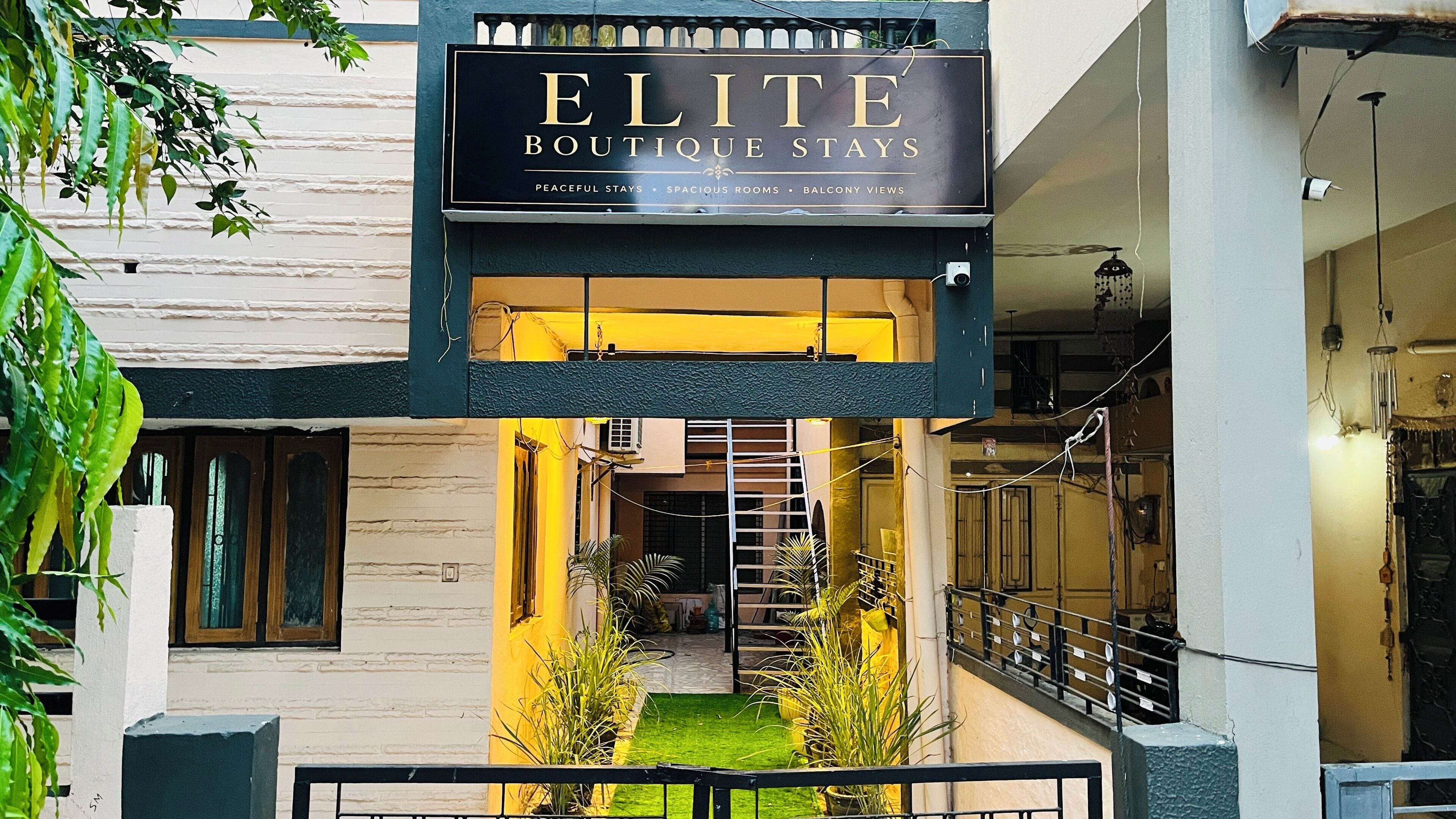 A boutique hotel named 'ELITE' with a sign indicating 'PEACEFUL STAYS,' 'SPACIOUS ROOMS,' and 'BALCONY VIEWS.'