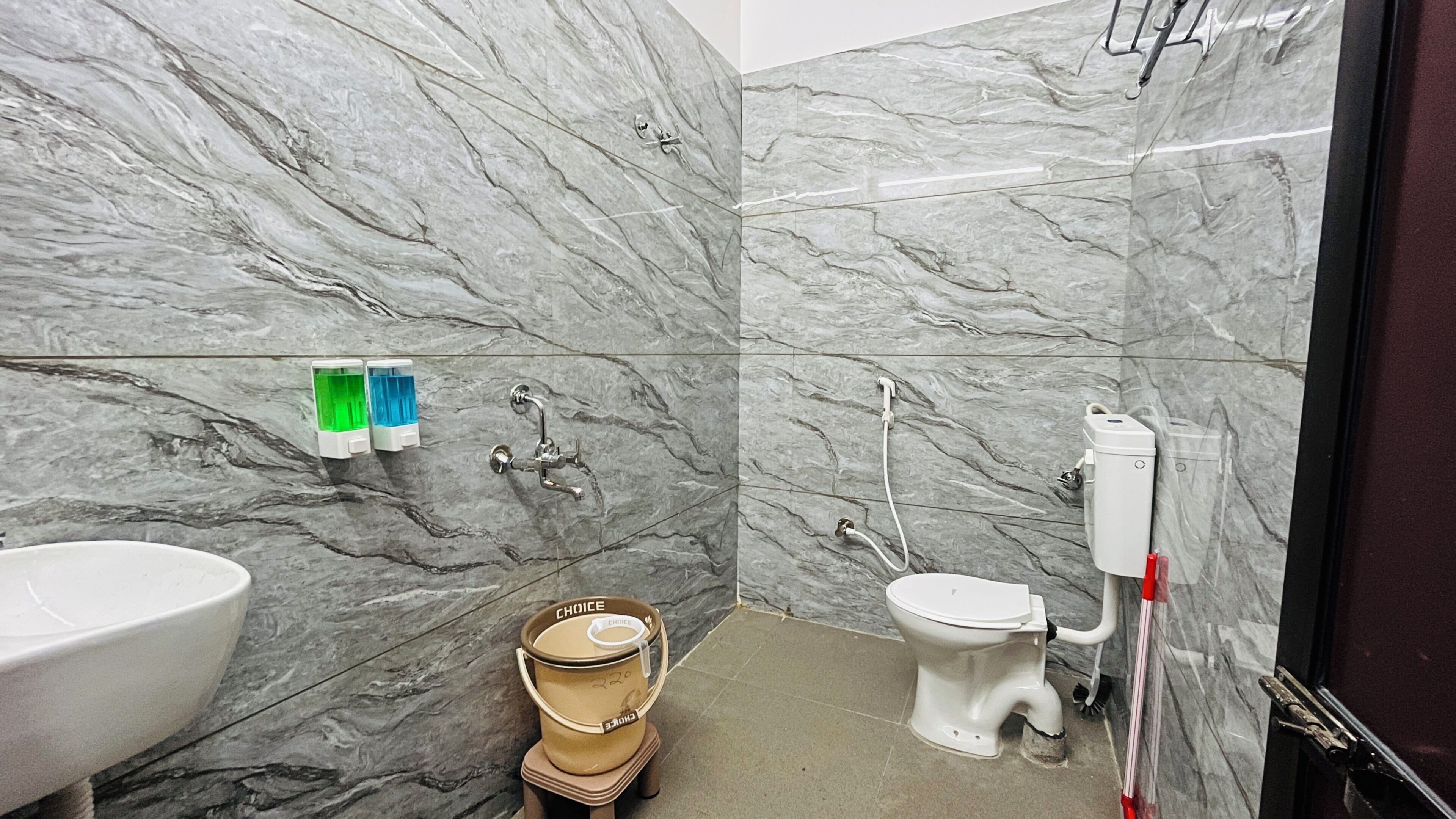 A bathroom with marble walls, a toilet, a bidet, a bidet brush, and a sink.