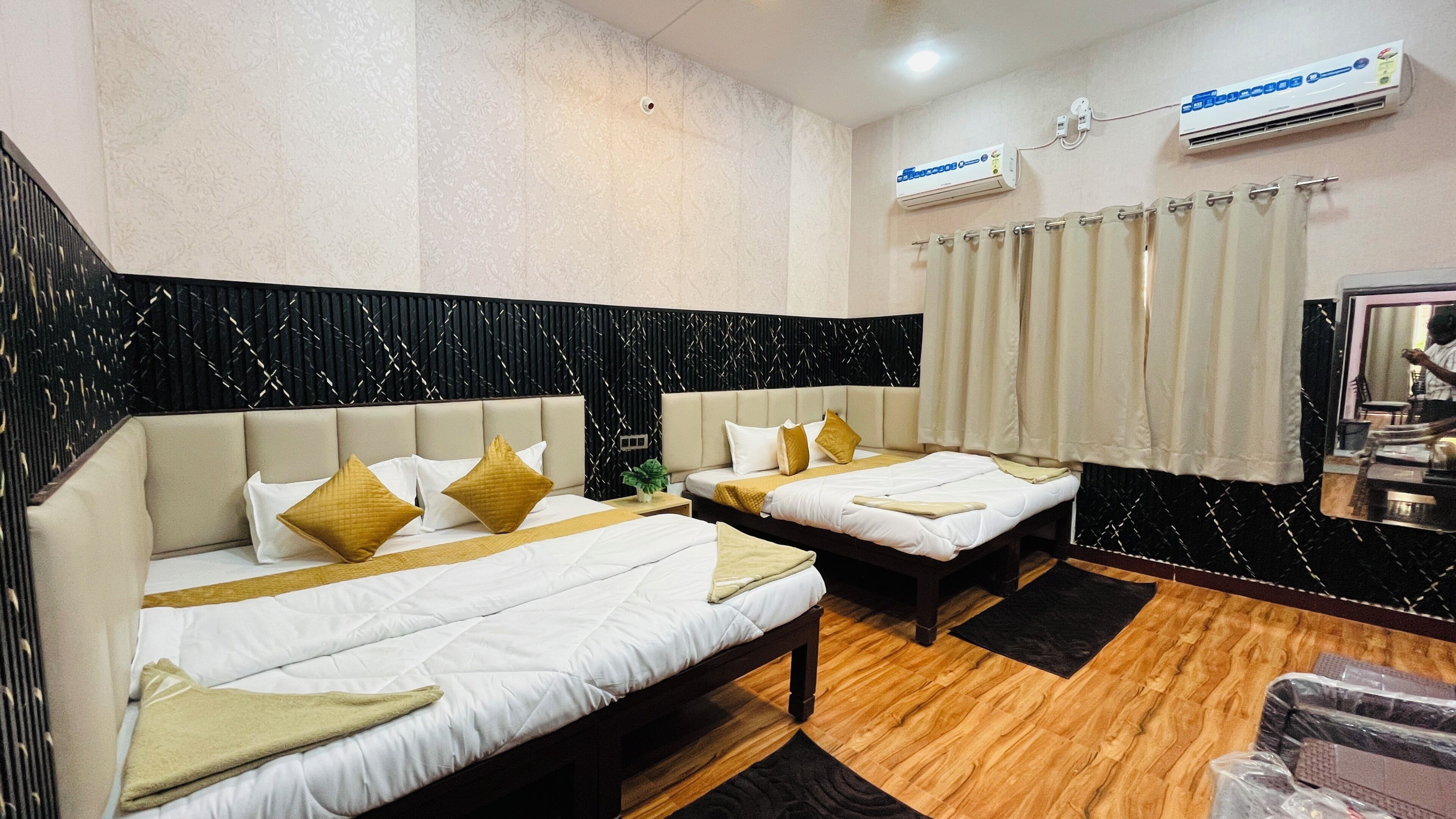 Habitación de hotel con dos camas, cabecera con estampado blanco y negro, unidad de aire acondicionado, espejo y piso de madera.