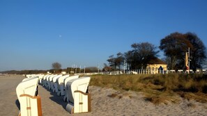 Ein Strand mit Reihen weißer Liegen und ein Gebäude mit gelbem Dach im Hintergrund.