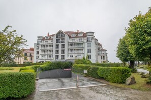 Ein mehrstöckiges Gebäude mit Balkonen, umgeben von gepflegten Hecken und Bäumen.