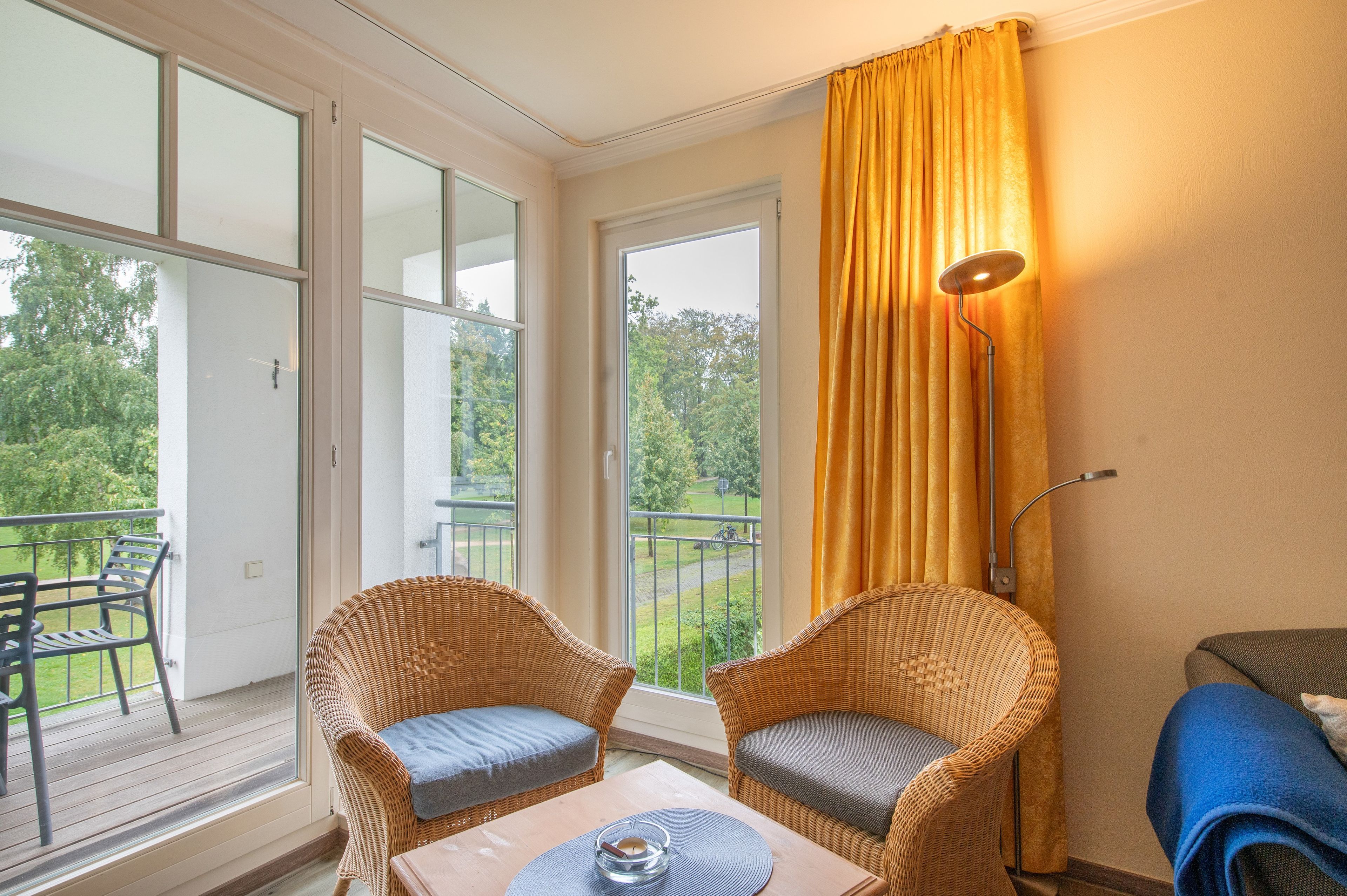 Un balcon avec des fauteuils en osier, une table et une vue sur la verdure.