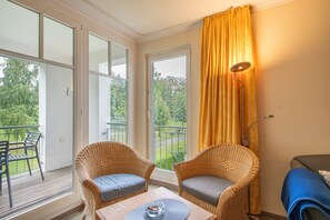 Ein Balkon mit Korbstühlen, einem Tisch und Blick auf Grünflächen.