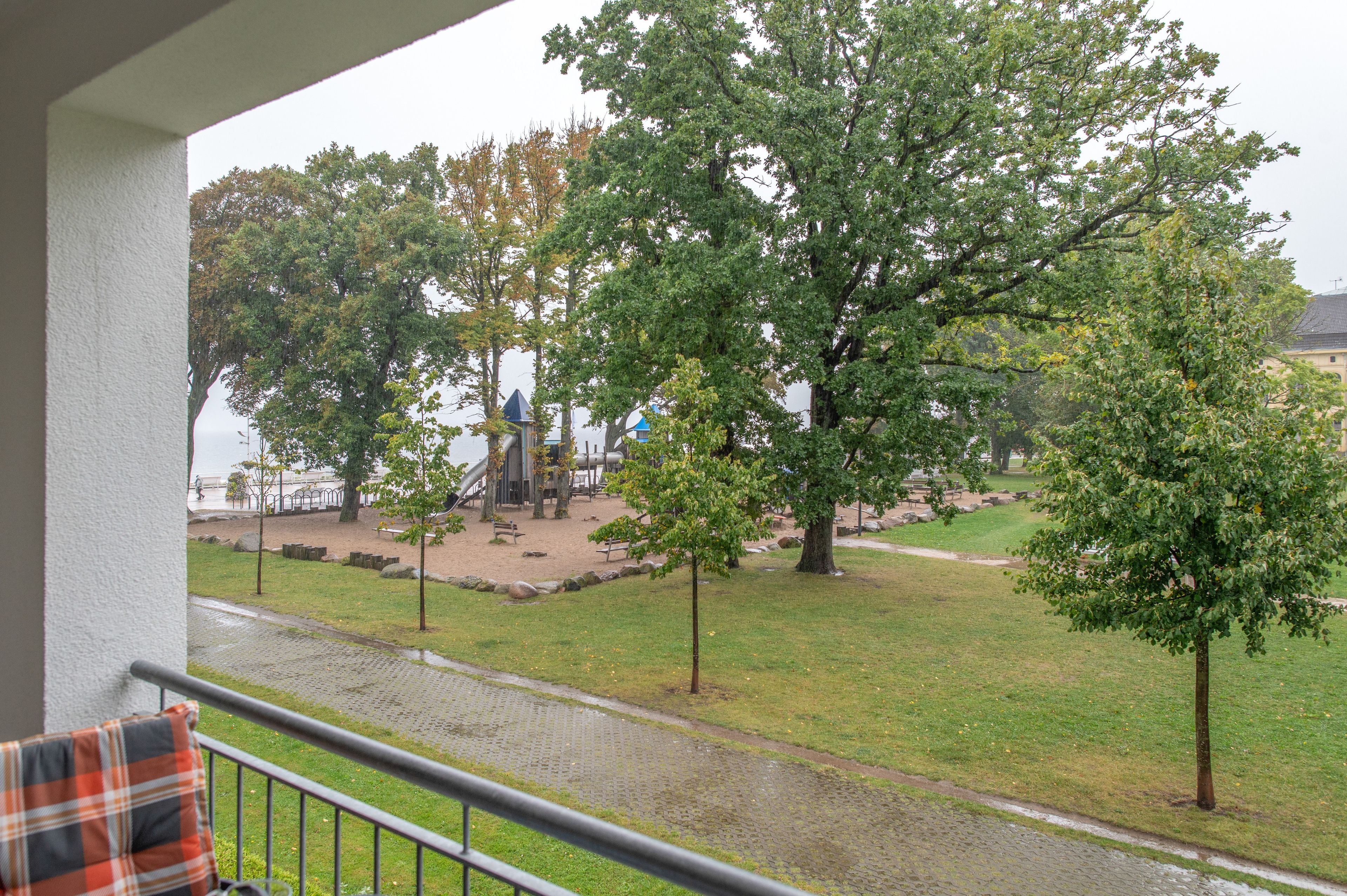 A view from a balcony overlooking a park with trees, a playground, and a body of water.