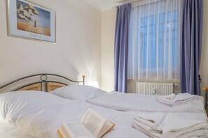 Ein Hotelzimmer mit zwei Betten, einem fensterbelaubten Fenster, einem Heizkörper und einem Bild an der Wand.