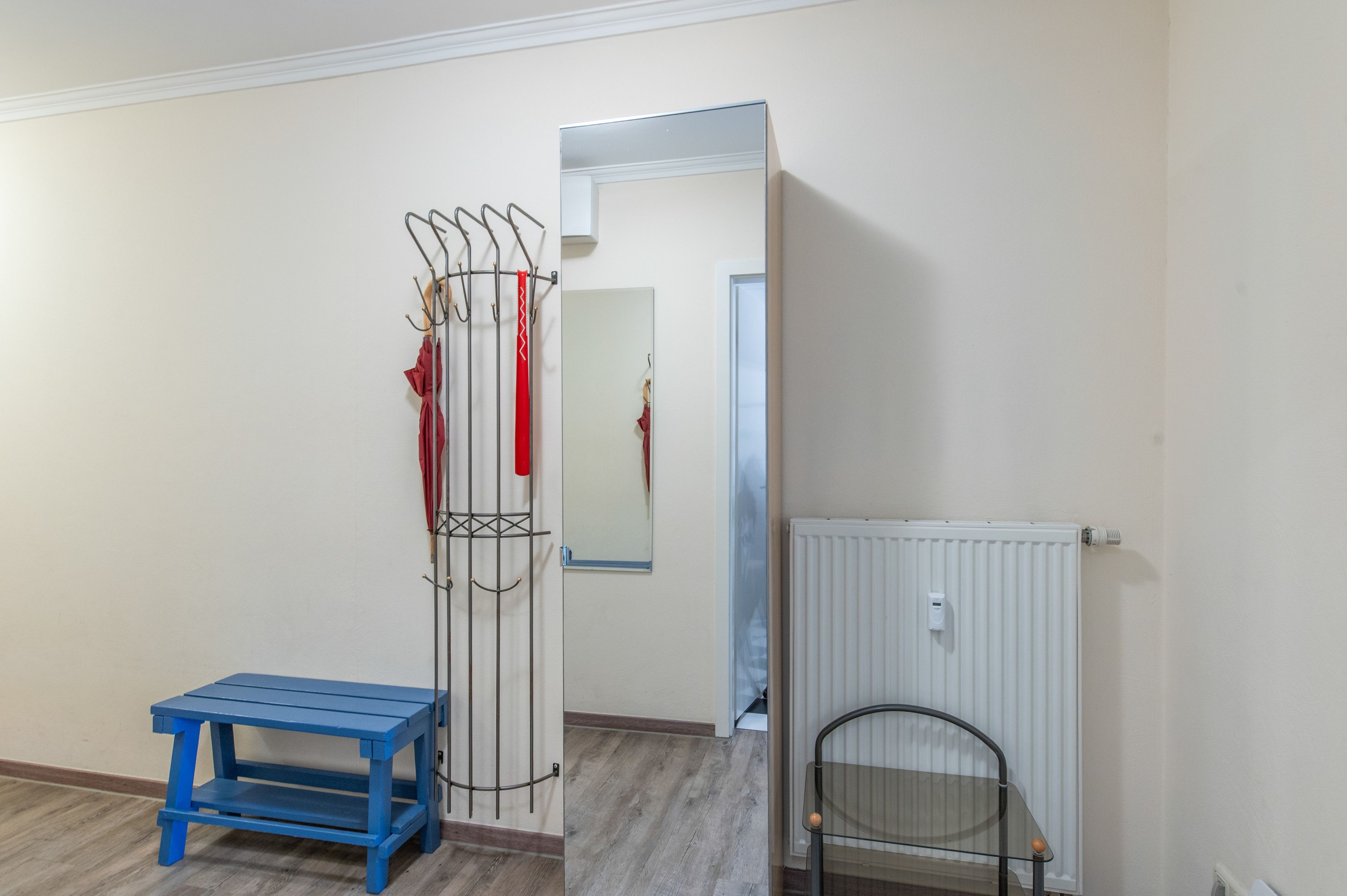 Ein Zimmer mit Kleiderhaken, einer blauen Bank, einer Heizung und einer Tür zu einem weiteren Raum.