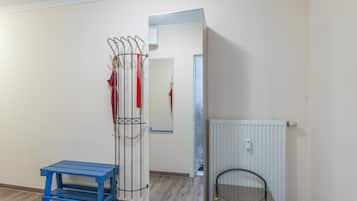 Ein Zimmer mit Kleiderhaken, einer blauen Bank, einer Heizung und einer Tür zu einem weiteren Raum.