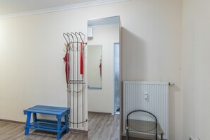 Ein Zimmer mit Kleiderhaken, einer blauen Bank, einer Heizung und einer Tür zu einem weiteren Raum.