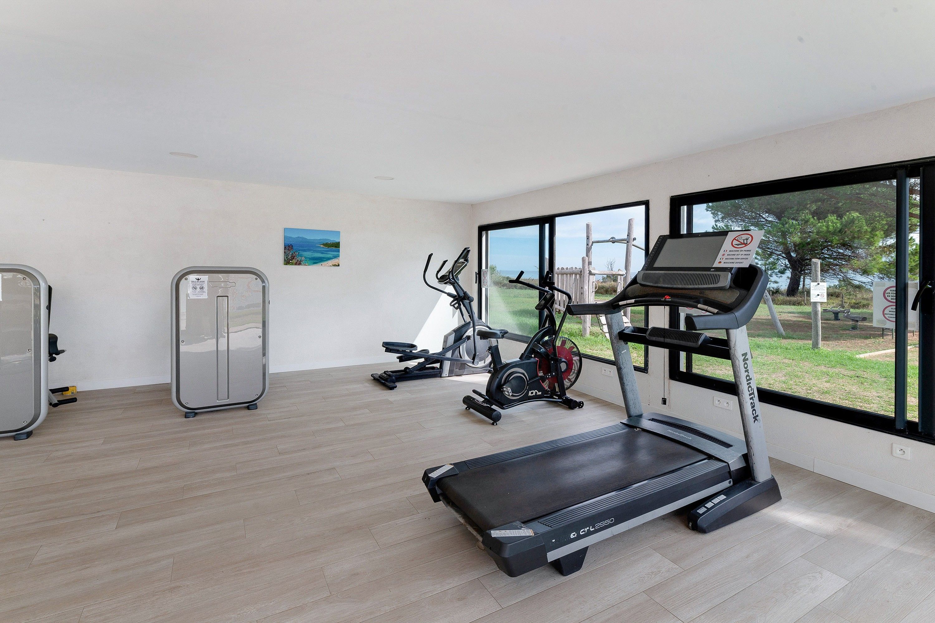 A gym with cardio machines, a weight bench, and a large window with a view of the outdoors.