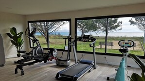 A home gym with exercise equipment, large windows, and a view of a grassy area.