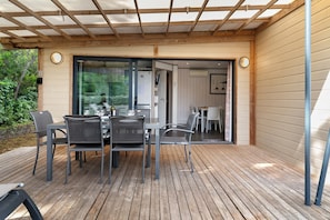 An outdoor patio with a table and chairs, a wooden deck, and a glass door leading to an interior space.