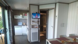 A compact room with a kitchenette, a dining area with a table and chairs, and a TV mounted on a wall.