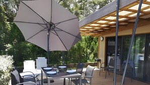 An outdoor deck with a table and chairs, a large umbrella, and a pergola structure.