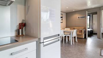 A modern kitchen with a refrigerator, a dining table with chairs, and a living area with a sofa and a window.