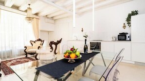 A dining area with a glass table, chairs, a chandelier, and a kitchen in the background. - The Muse... (Venice)