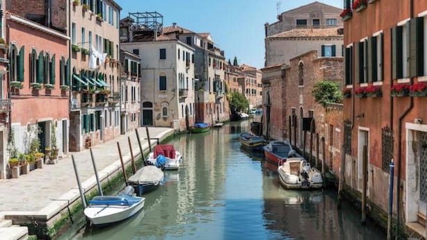 A narrow canal flanked by historic buildings with boats docked along the sides. - The Muse... (Venice)