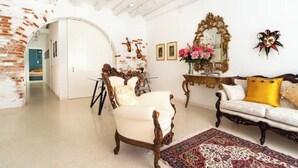 A room with a white door, a wooden chair, a sofa with a yellow pillow, a mirror, and a patterned rug. - The Muse... (Venice)
