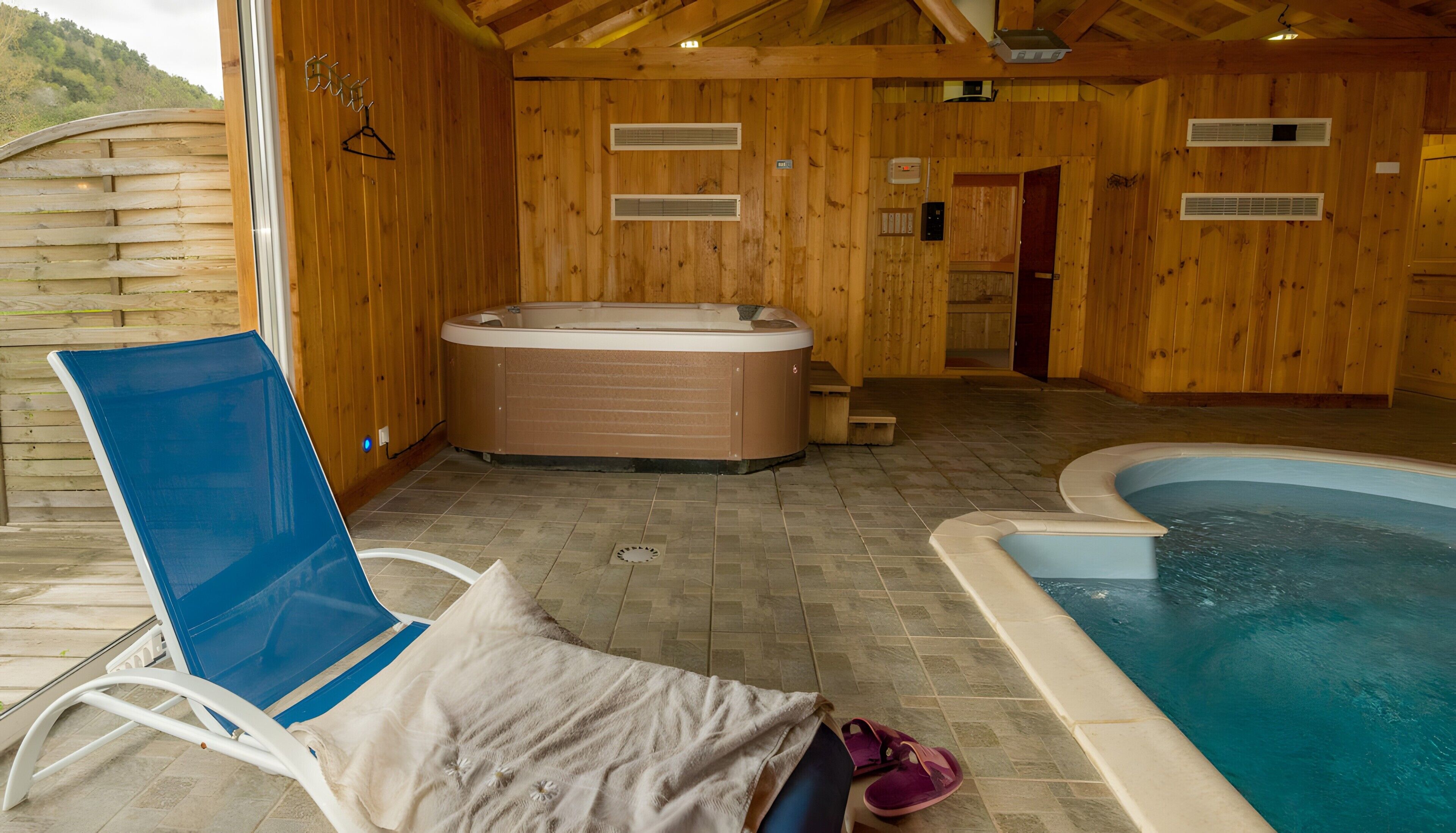 Ein Spa-Raum aus Holz mit Whirlpool, Schwimmbecken und Liegestuhl.
