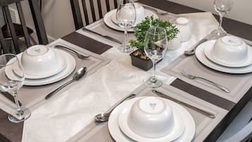 A dining table set with white plates, bowls, and wine glasses, accompanied by a small potted plant and salt and pepper shakers.