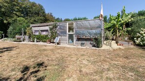 A rustic house with a large greenhouse, surrounded by a garden with various plants and trees. - Caravan in a Small Garden Oasis (Brix)
