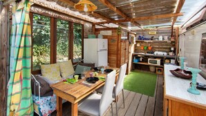 A rustic cabin interior with a wooden dining table, chairs, a kitchen area with a sink and appliances, and a cozy seating area with cushions. - Caravan in a Small Garden Oasis (Brix)