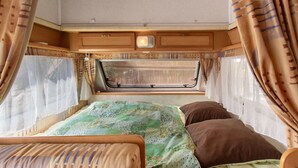 A compact RV interior with a bed, a window, and a small kitchenette area. - Caravan in a Small Garden Oasis (Brix)