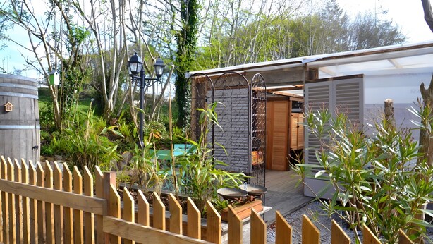 A wooden fence, a metal gate, a wooden shed, and a house with a garage. - Caravan in a Small Garden Oasis (Brix)