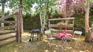 A rustic outdoor seating area with a wooden table and chairs, a small table with a lantern, and a wooden bench with a red cloth.