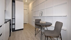 A modern kitchen with a round table and two chairs, a white wall with a shelf, and a door leading to another room. - Modern Studio Apartment in the City Centre (Yerevan)