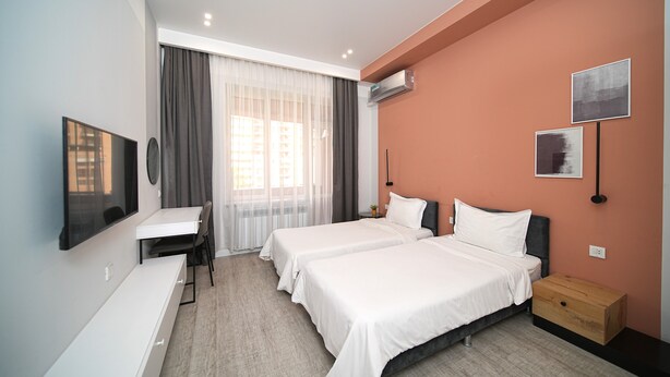 A hotel room with two beds, a desk, a TV, and a window with curtains. - Modern Studio Apartment in the City Centre (Yerevan)