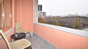 A balcony with two wicker chairs and a small table, overlooking a cityscape with buildings and trees. - Modern Studio Apartment in the City Centre (Yerevan)