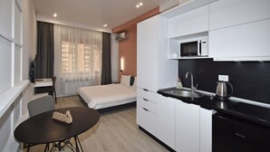 A modern hotel room with a bed, a desk, a dining table, a kitchen area with a microwave, sink, and kettle. - Modern Studio Apartment in the City Centre (Yerevan)