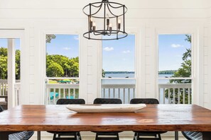 A dining area with a wooden table and chairs, a chandelier, and large windows with a view of the water. - Lake Lyfe Oconee - Game Room, Dock, Firepit (Eatonton)