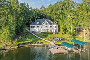 A large house with a dock and a small boat, surrounded by dense trees and a body of water. - Lake Lyfe Oconee - Game Room, Dock, Firepit (Eatonton)