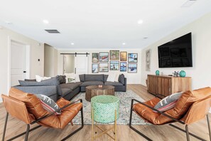 A modern living room with a sectional sofa, leather armchairs, a coffee table, and a TV mounted on the wall. - Lake Lyfe Oconee - Game Room, Dock, Firepit (Eatonton)