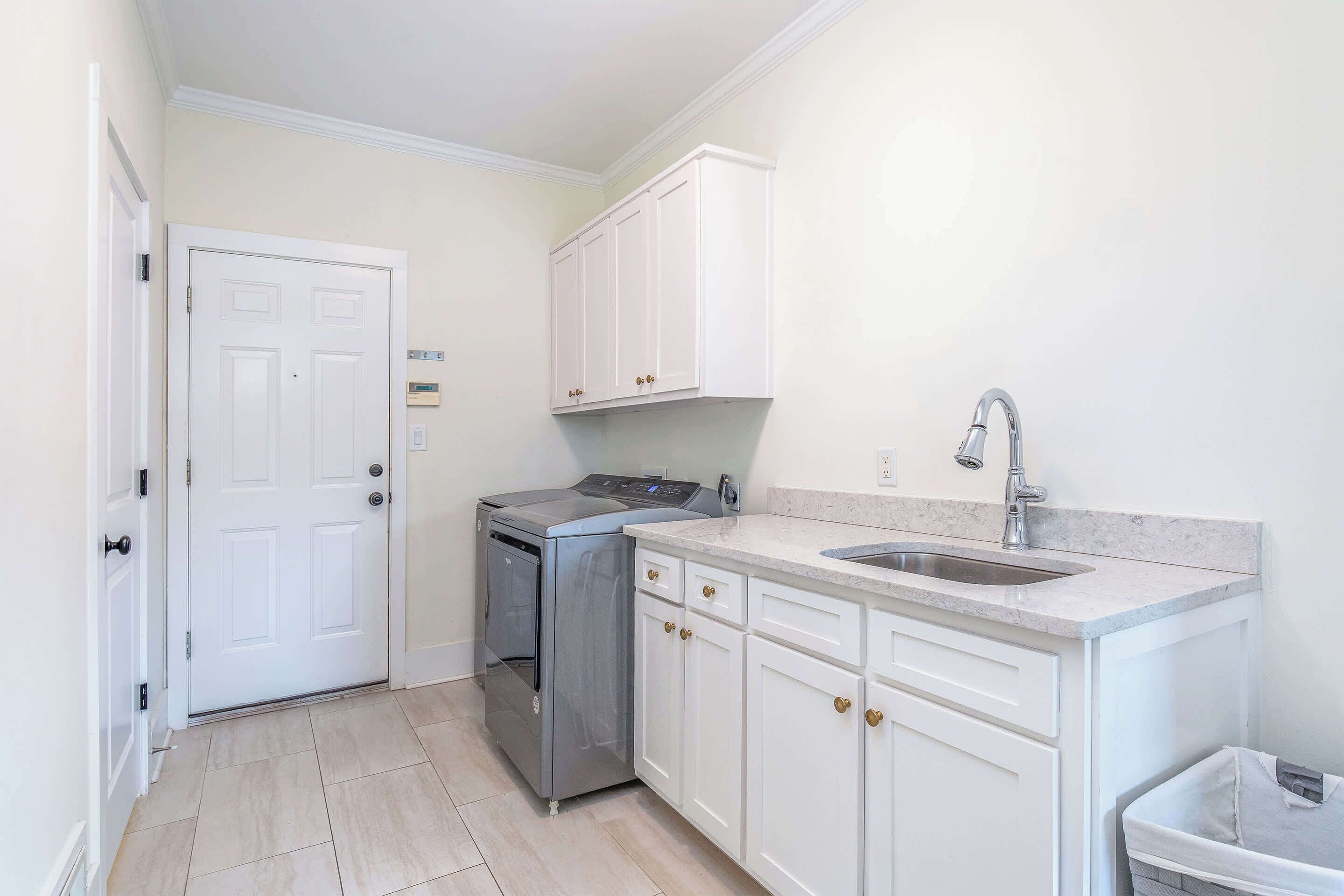 A kitchen with white cabinets, a stainless steel oven, a sink with a modern faucet, and a trash bin.
