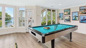 A pool table in a room with large windows, a door leading outside, and several framed pictures on the wall. - Lake Lyfe Oconee - Game Room, Dock, Firepit (Eatonton)