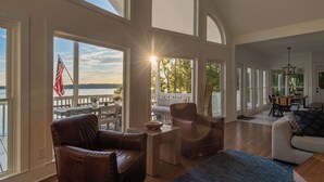 A spacious living room with large windows, a leather armchair, a wooden coffee table, and a view of the outdoors. - Lake Lyfe Oconee - Game Room, Dock, Firepit (Eatonton)