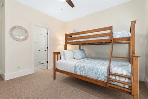 Ein Stockbett mit Holzrahmen und gemusterten Betttextilien, ein runder Spiegel an der Wand und eine Tür zu einem weiteren Zimmer.