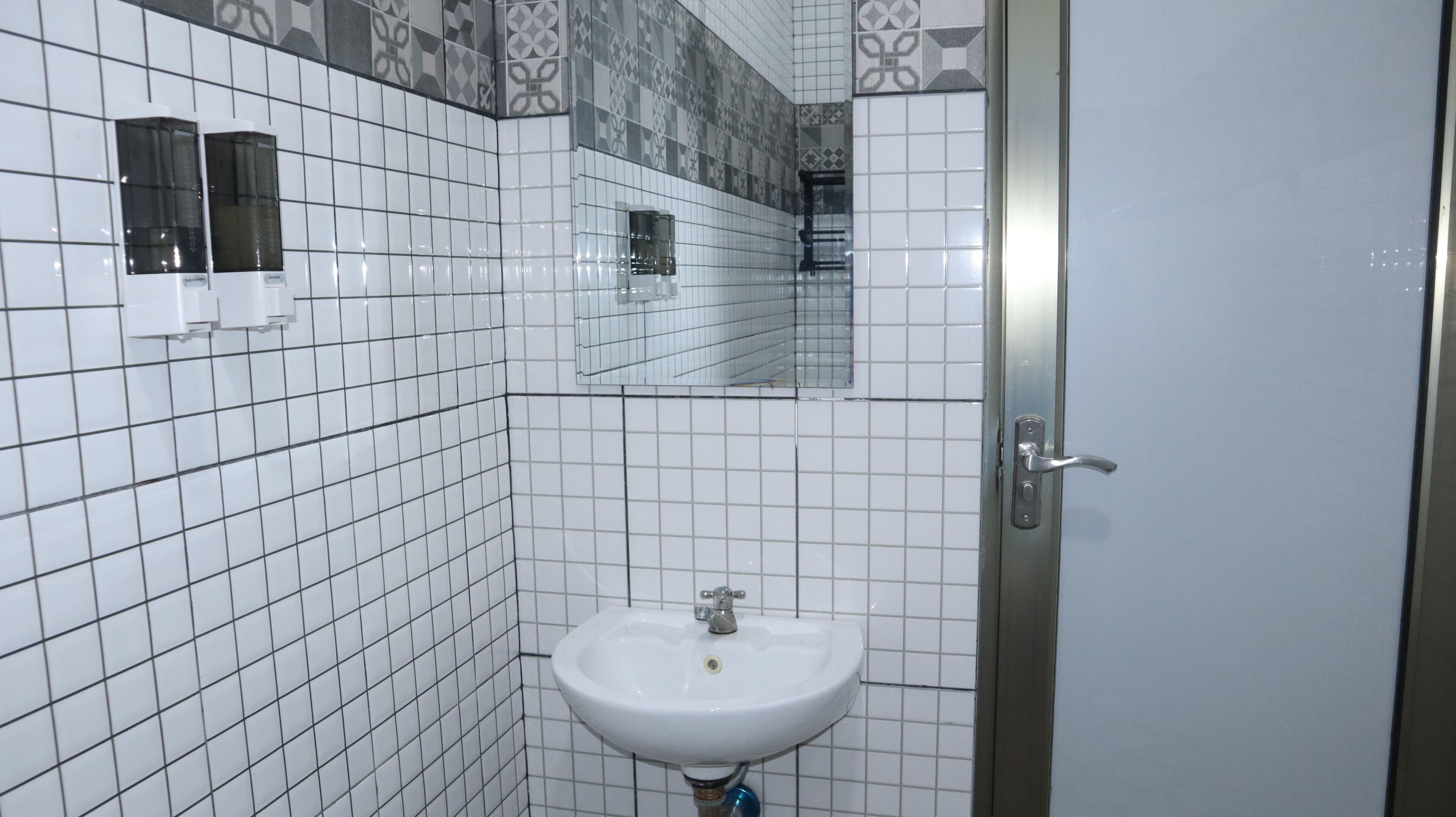 A bathroom with white tiled walls, a white sink, and a mirror.