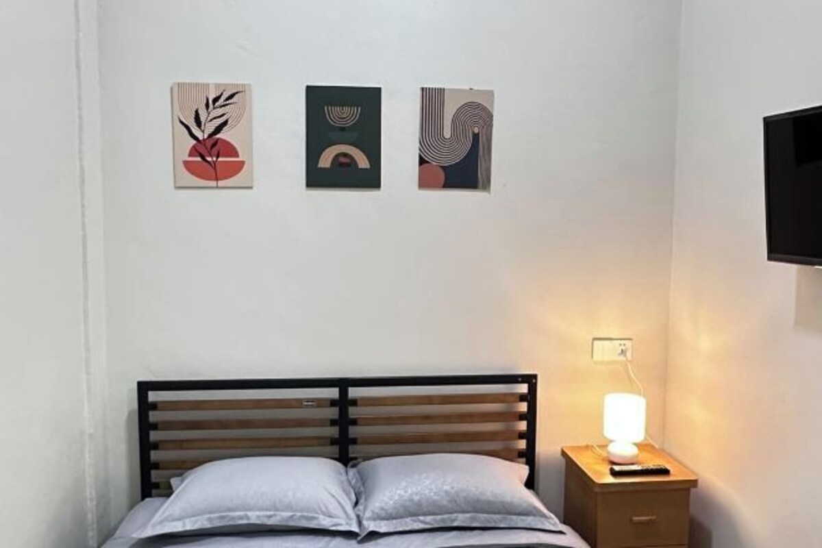 Un dormitorio con una cama, una mesita de noche con lámpara y tres obras de arte colgadas en la pared.