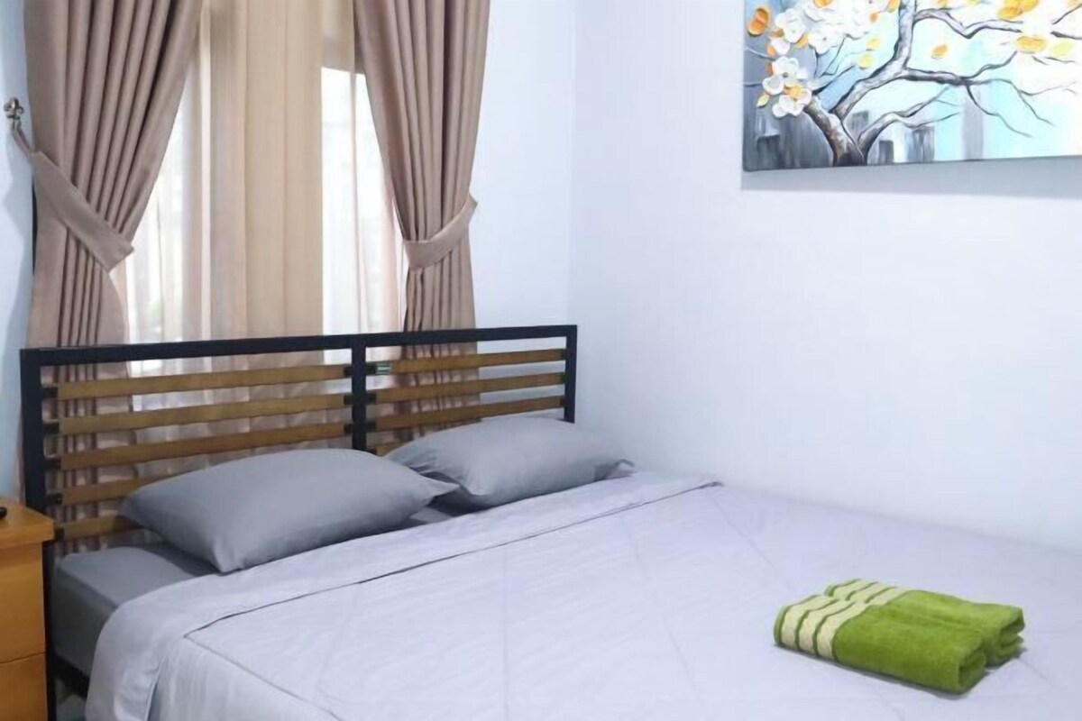 A bed with a wooden headboard, grey bedding, and a green towel on the floor.