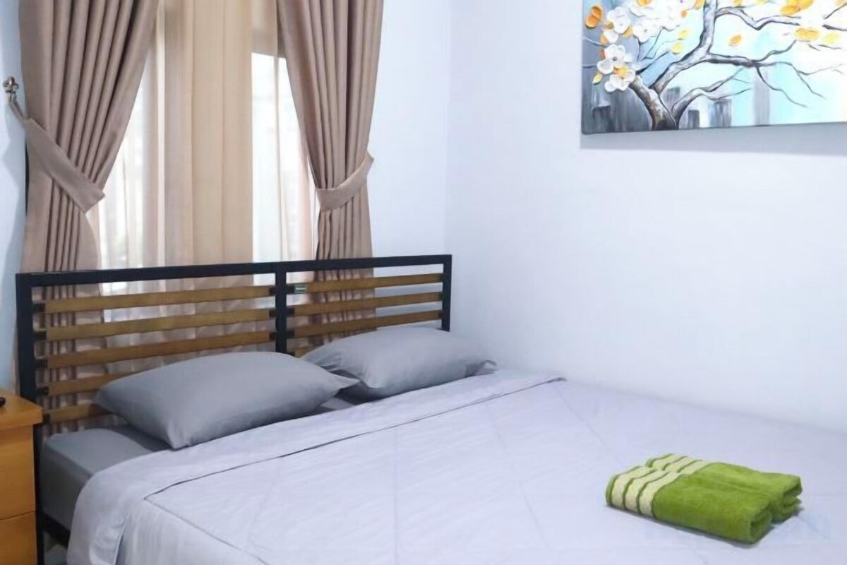 Un dormitorio con una cama, cortinas, un cuadro y una toalla verde sobre la cama.